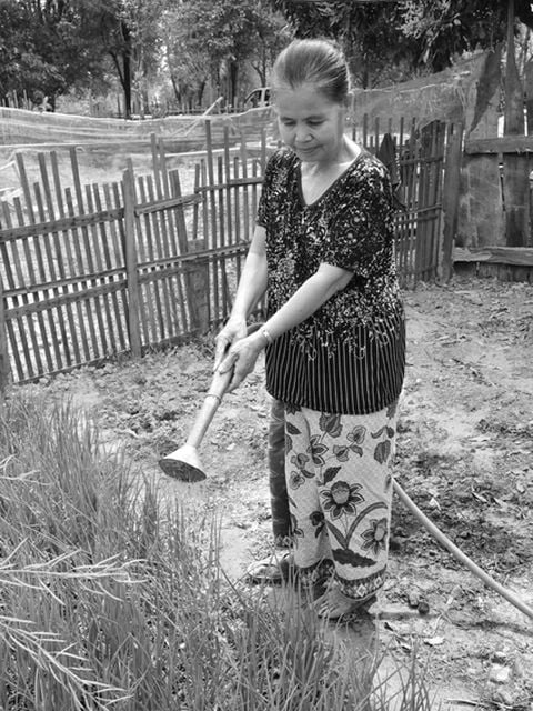 Phet Laktasabout gießt das Beet vor ihrem Haus.