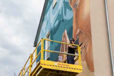 Graffiti Künstler AKUT sprüht sein Kunstwerk von einer Hebebühne aus in Augsburg.