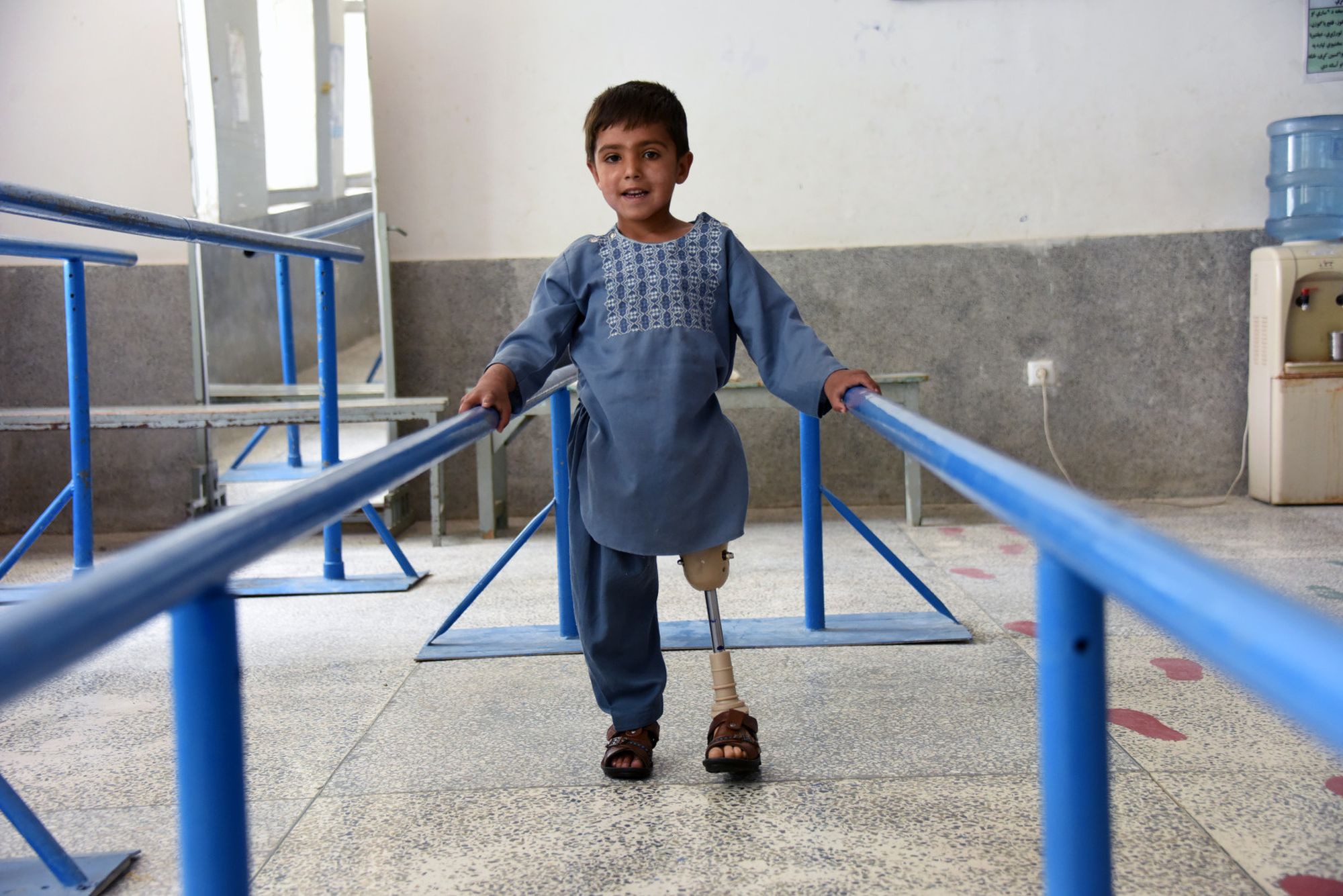Ein Junge aus Afghanistan übt an Handläufen mit seiner Prothese zu gehen.