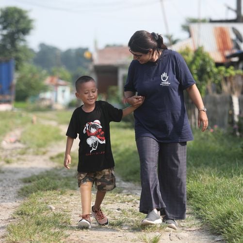 Ein Junge aus Nepal geht mit seiner Prothese an der Hand einer HI-Physiotherapeutin