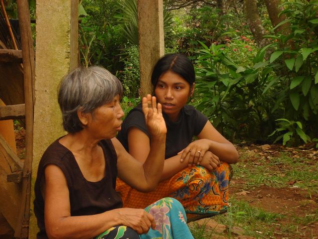 Die gehörlose Sopheak sitzt mit ihrer Großmutter vor ihrem Haus. Sopheak sieht ihre Großmutter an, die gerade eine Gebärde macht.