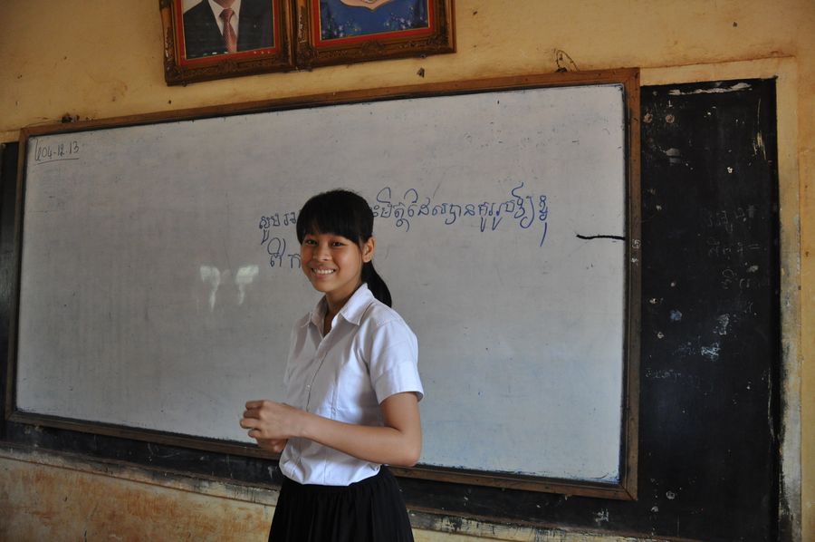 Kanha lächelnd in einem Klassenzimmer vor einer Tafel in Schuluniform. 