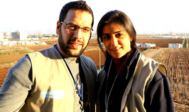 Cynthia und Elias, Physiotherapeutin und Sozialarbeiter von Handicap International in Libanon, schauen in die Kamera, im Hintergrund ist ländliches Gebiet.