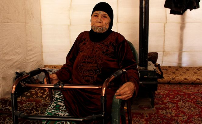 Fteim sitzt in einem Zettel in einer Flüchltingseinrichtung in Libanon. Sie hält sich an einer Gehhilfe fest. 