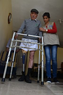 Mahmoud steht aufgestützt auf seinem Gehgestell und wird dabei von der Physiotherapeutin unterstützt.