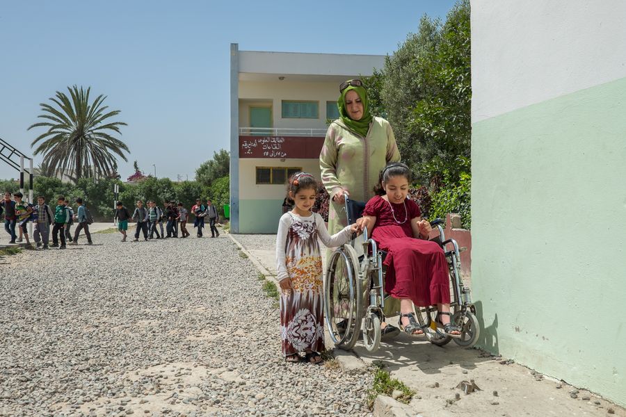 Ikram gemeinsam mit ihrer Mutter und ihrer Schwester auf dem Heimweg. Der Weg besteht aus Geröll, nur ein kleiner Streifen ist für sie im Rollstuhl befahrbar.