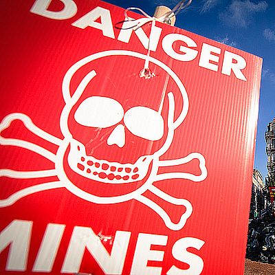 Antilandmine-HI Zu sehen ist ein Danger Mines Zeichen mit einer Protestschuhpyramide im Hintergrund und einem Handicap International Emblem auf der Spitze.