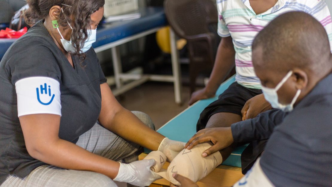 Zwei HI-Mitarbeitende helfen einem Mann mit der Bandage um sein amputiertes Bein.