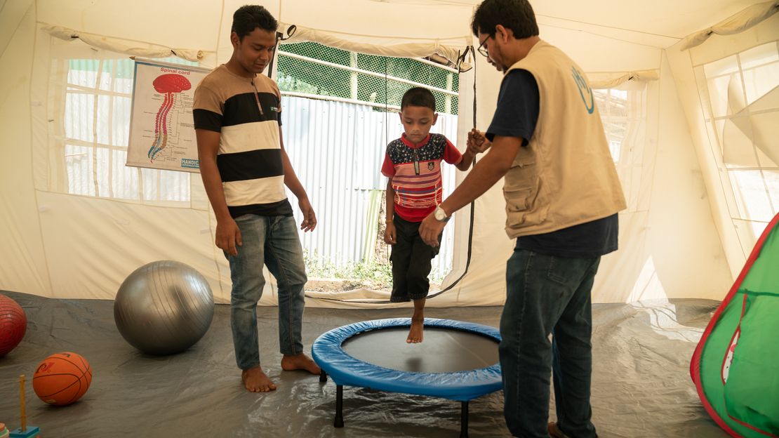 Auf dem Bild ist Anowar mit seinem Physiotherapeuten Redowan und seinem Bruder Guramia bei einer Rehabilitationsübung zu sehen. zu sehen. 