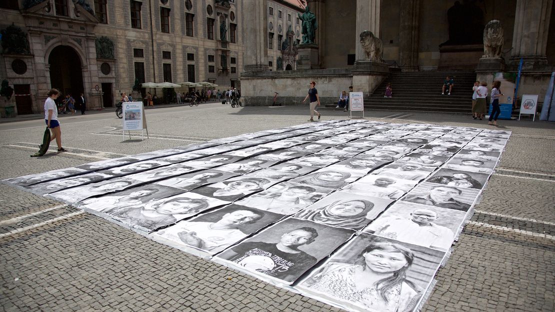 Achtzig schwarzweiß Portraits von verschiedenen Menschen liegen auf dem Boden am Münchner Odeonsplatz 
