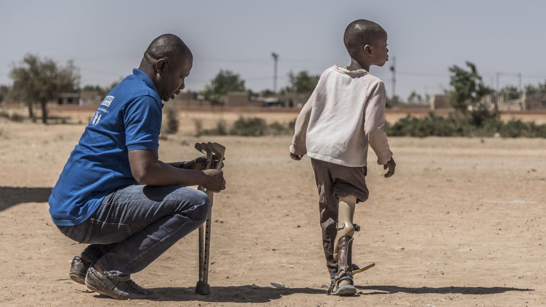 Ein HI-Helfer kniet in Burkina Faso vor einem Jungen, der von HI eine Prothese bekommen hat.