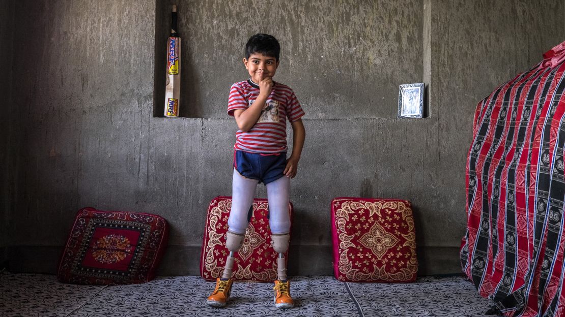 Fayaz sitzt mit seinen neuen Prothesen und einem Mitarbeiter von Handicap International auf einer Steinmauer.