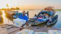 Ein Mann entlädt Hilfspakete von einem Boot auf einem Fluss. Im Hintergrund geht die Sonne unter. 