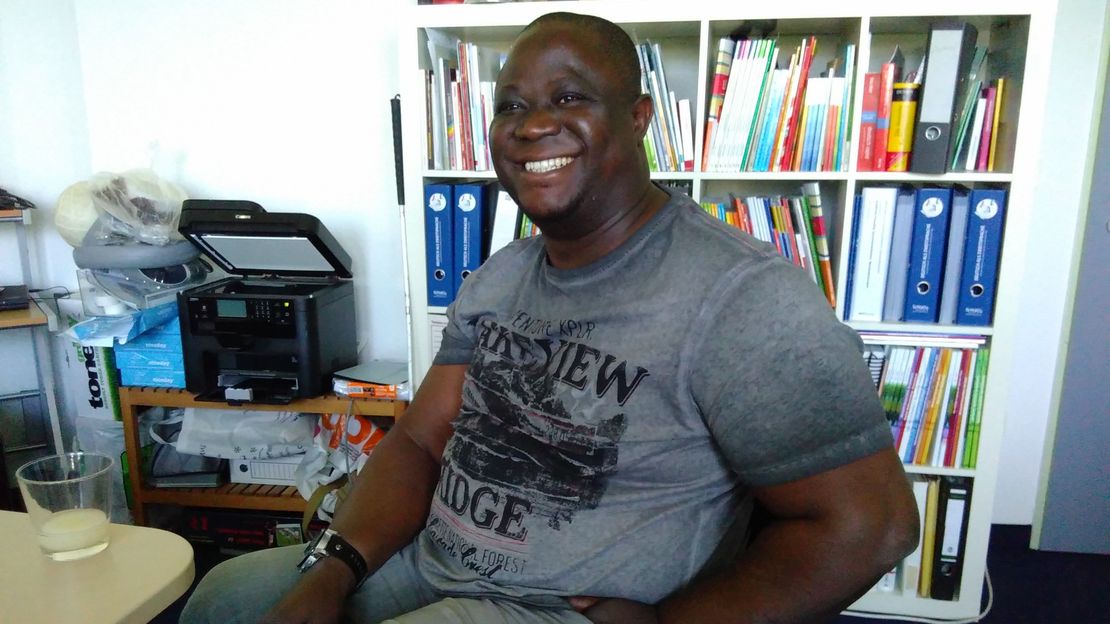 Samuel Jerry Ubi sitzt im Rollstuhl in einem Büro und lächelt.