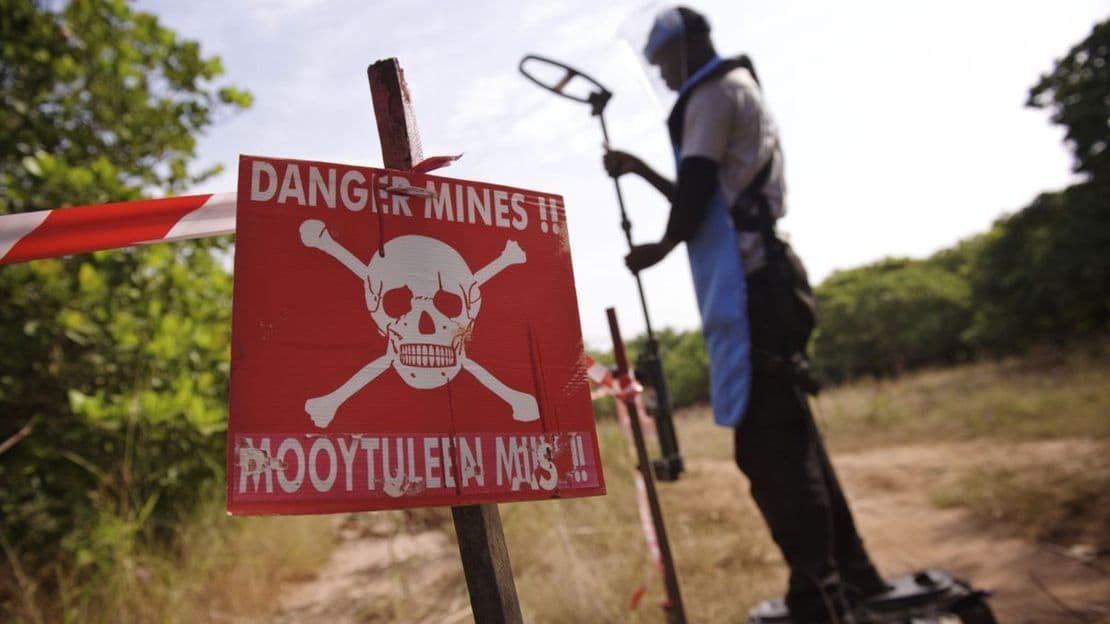 Ein Mann mit blauer Schutzkleidung und Metalldetektor steht hinter einem roten Totenkopfschild mit der Aufschrift 