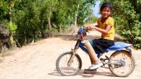 Sreyka aus Kambodscha sitzt mit ihrer Prothese am linken Bein auf einem Fahrrad und lacht in die Kamera.