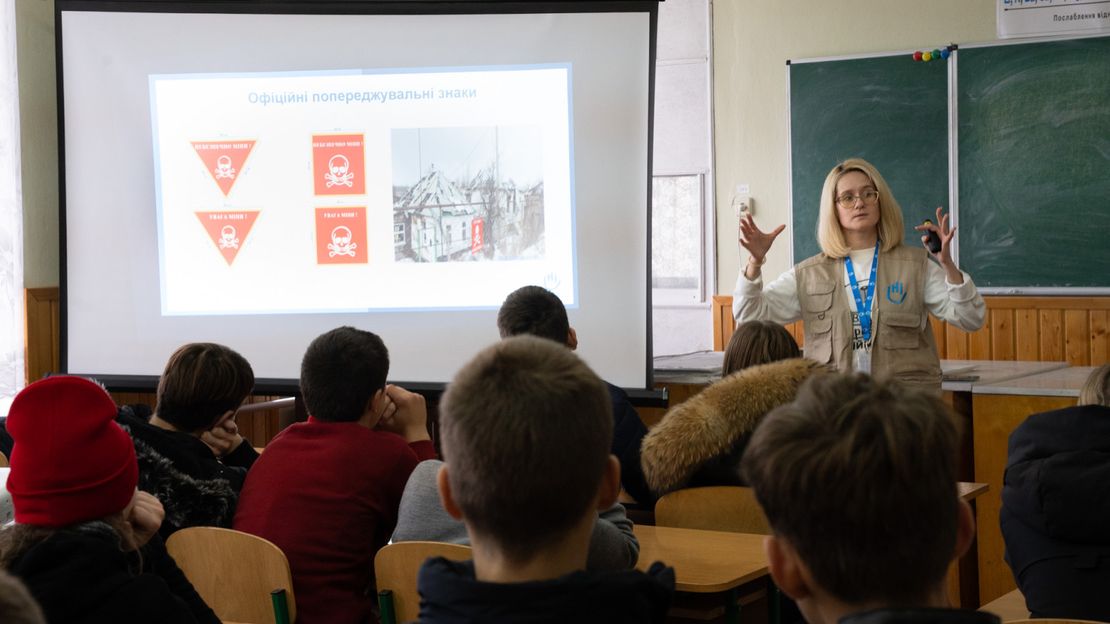 Eine Lehrerin klärt Schulkinder über die Gefahren von Streumunitionen auf