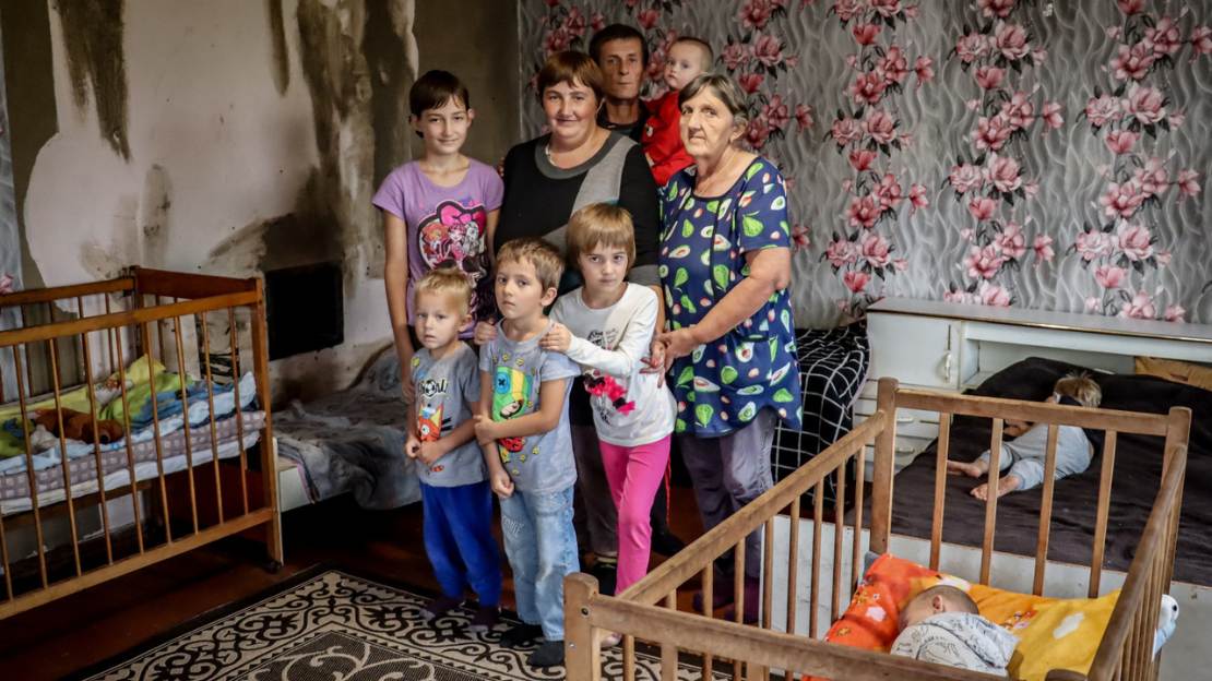 Familie Vektov steht in ihrem Wohnzimmer und schaut in die Kamera.