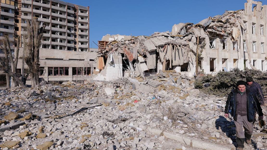 Zwei Männer stehen vor einem zerbombten Wohnhaus in der Ukraine