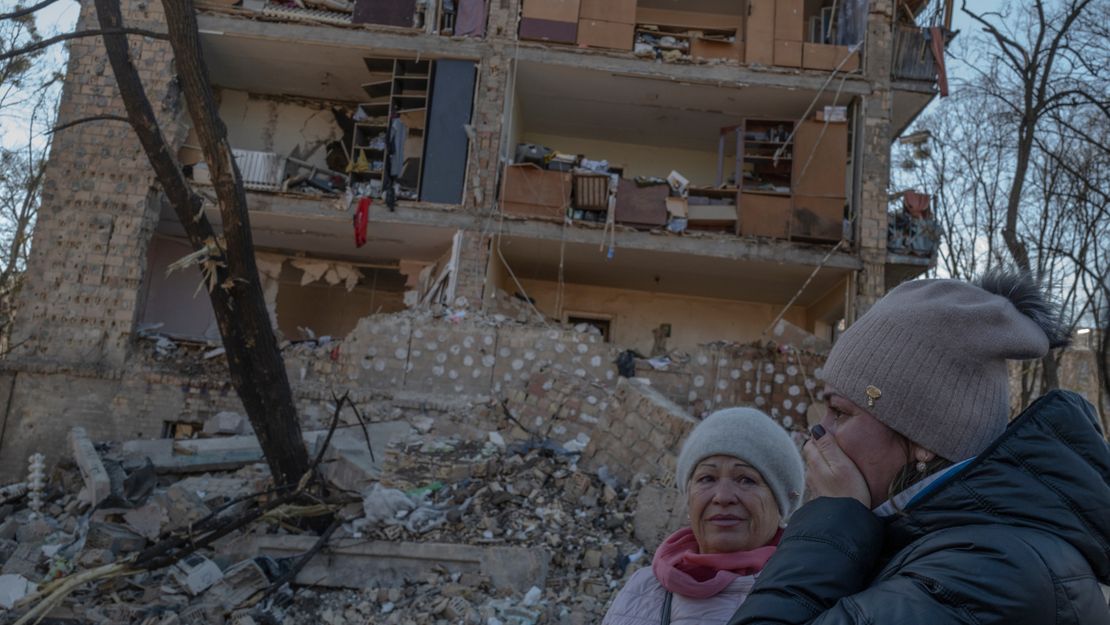 Zwei Frauen stehen vor den Trümmern eines zerbombten Hauses in der Ukraine. 