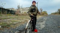 Nazar, 11, steht mit seinem Fahrrad vor seiner zerbombten Schule.
