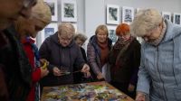Eine Gruppe von älteren Damen steht um einen Tisch, auf dem bunt bedruckte Karten liegen. Sie schauen die Karten genau an und nehmen sie in die Hand. 