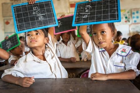 Zwei Mädchen in Kambodscha in der Schule, die eine Schreibtafel hochhalten.