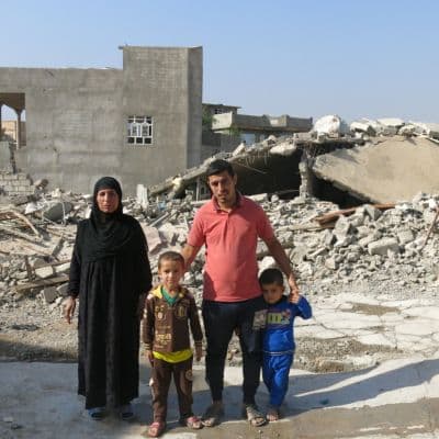 Eine Familie steht in einer zerstörten Wohnsiedlung. 