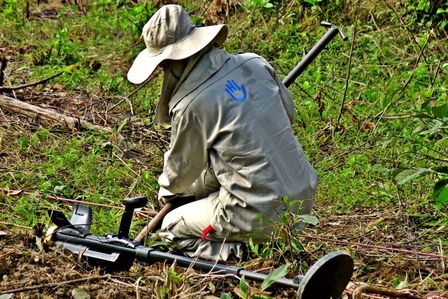 Ein Entminer legt in einem Feld in Laos eine Streubombe frei. Er ist von hinten zu sehen.