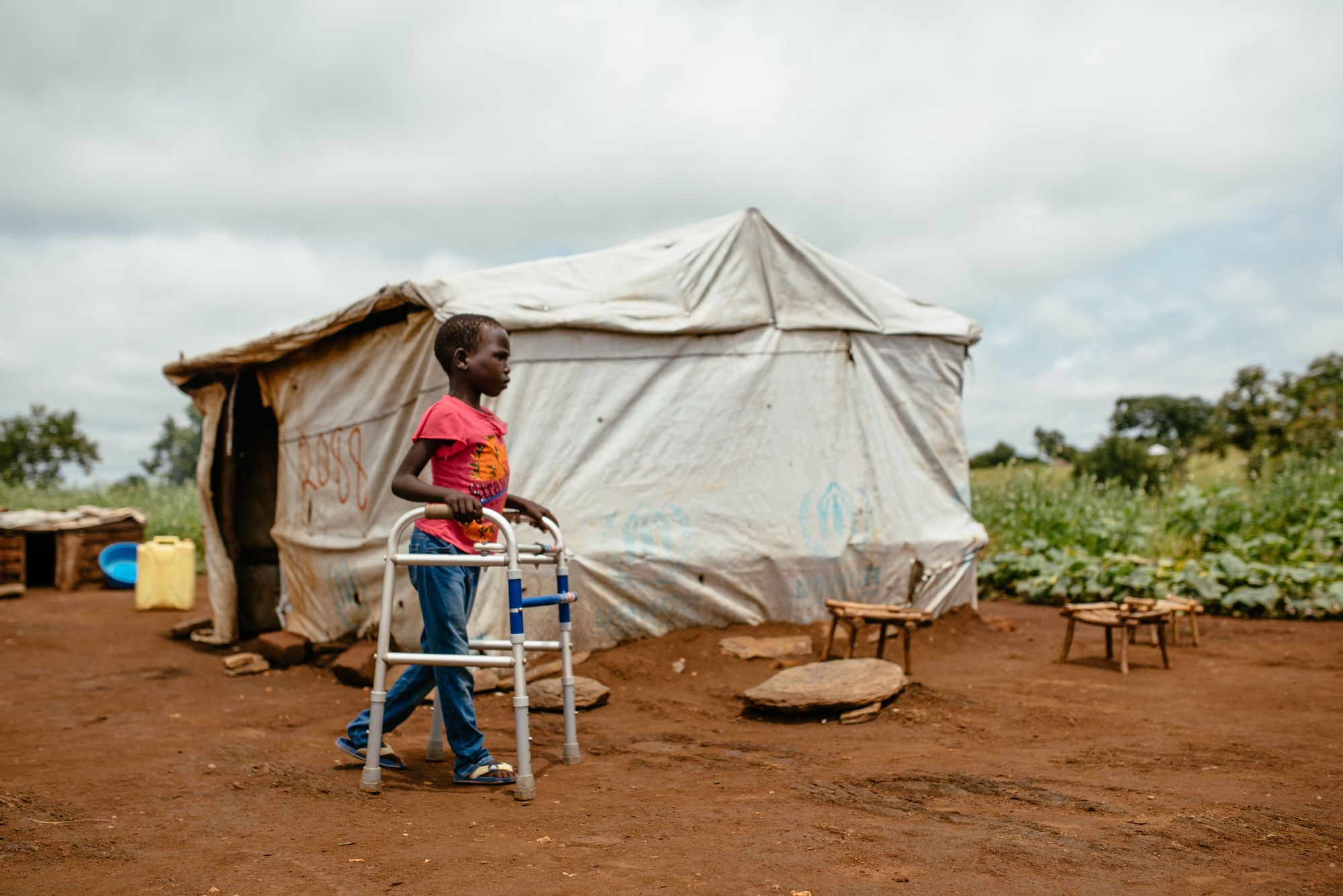 Junges Mädchen mit Gehilfe läuft vor einem Zelt in einem Geflüchtetenlager in Uganda.