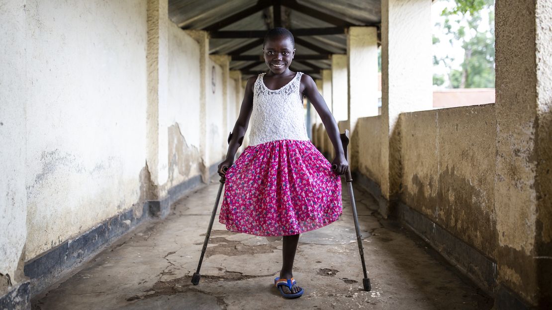 Kelvine aus der demokratischen Republik Kongo blickt lächelnd in die Kamera. Ihr fehlt ein Bein, sie stützt sich auf Krücken.