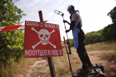 Ein Minenwarnschild im Vordergrund, ein Entminer in Ausrüstung im Hintergrund