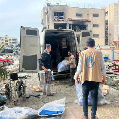 Männer laden einen Rollstuhl und andere Hilfsgüter aus einem Laster in Gaza. Im Hintergrund sind verwüstete Gebäude.