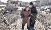 Ein älteres Ehepaar vor einem zerbombten Wohngebiet.; }}