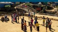 Menschen auf einem sandigen Platz in Bangladesch. Kinder spielen und die Eltern unterhalten sich. Die Kinder formen einen Kreise und halten sich an den Händen.; }}