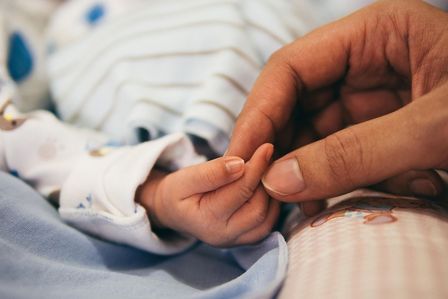 Die Hand einer Frau hält die eines neugeborenen Babys.