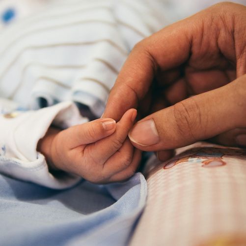 Die Hand einer Frau hält die eines neugeborenen Babys.