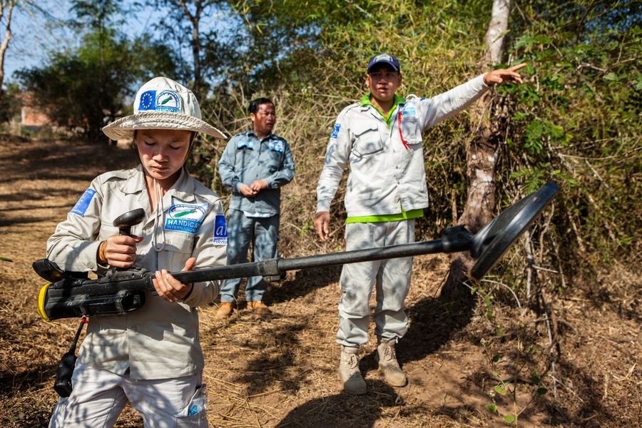 Zu sehen ist Lam in beieger Uniform von Handicap International. Sie trägt einen Minendetektor und befindet sich im Einsatzgebiet. 