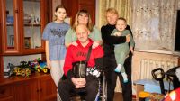 Nach einem Luftangriff 2022 in der Region Mykolajiw ist Oleksandr querschnittsgelähmt. Handicap International unterstützt ihn seitdem bei der Rehabilitation und mit Hilfsmitteln. Ein Mann im Rollstuhl ist umgeben von seiner Familie in einem Wohnzimmer.