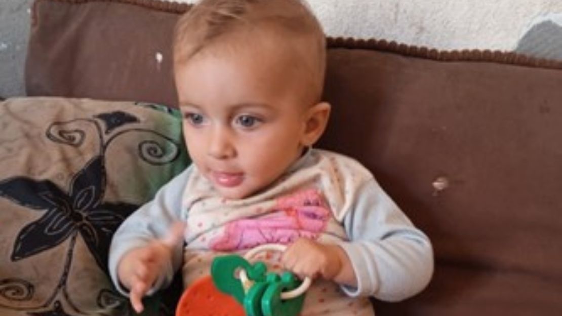 Ein Baby liegt auf einem Sofa und hält Spielzeug in der Hand. 
