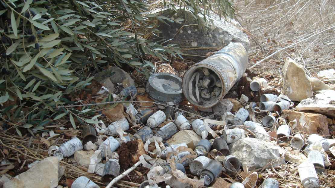 Ein geöffneter Streubombenblindgänger liegt zwischen Büschen. Überall liegt die Submunition verstreut.
