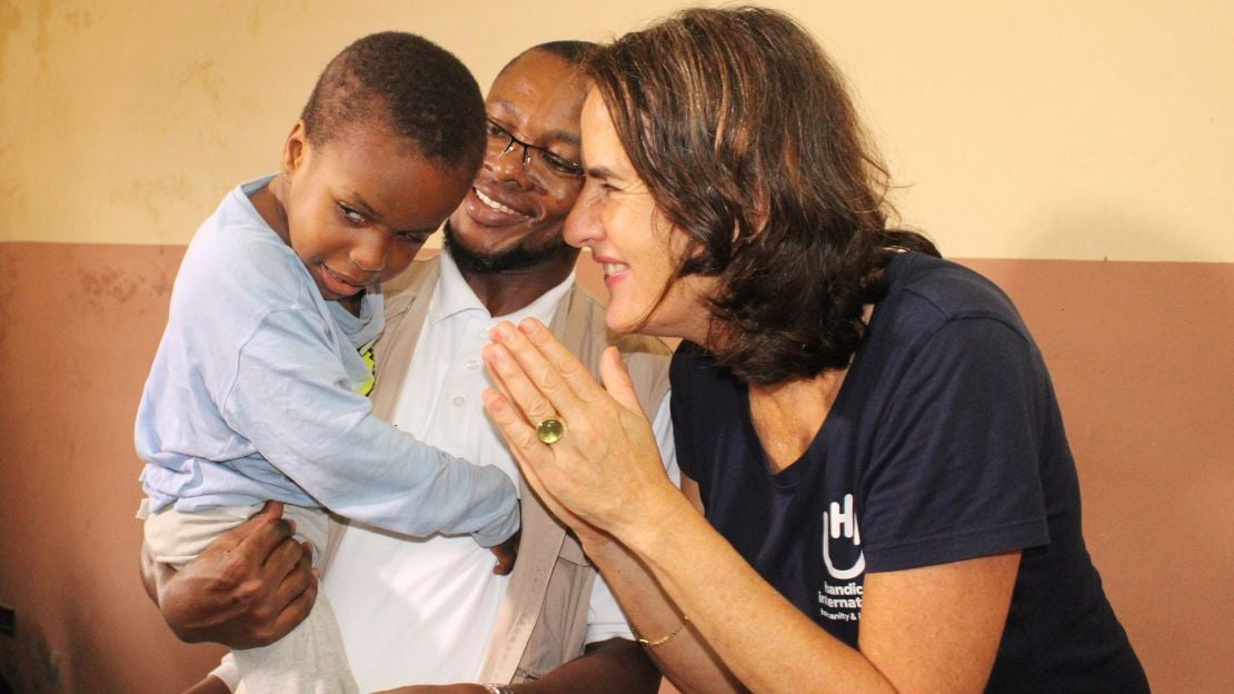 Uta Prehl beugt sich lächelnd zu einem kleinen Jungen, der von einem Mann auf dem Arm gehalten wird.