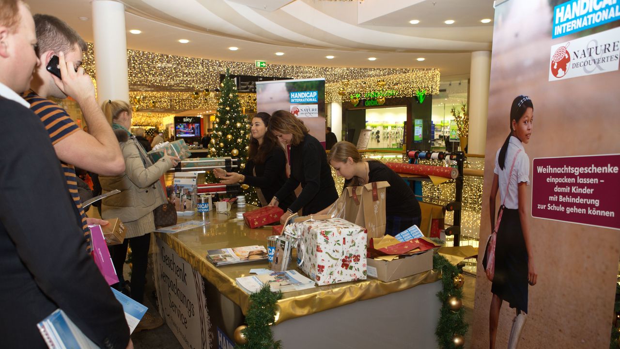 Mehrere Menschen stehen vor dem Stand von Handicap International. Einige packen Geschenke ein.