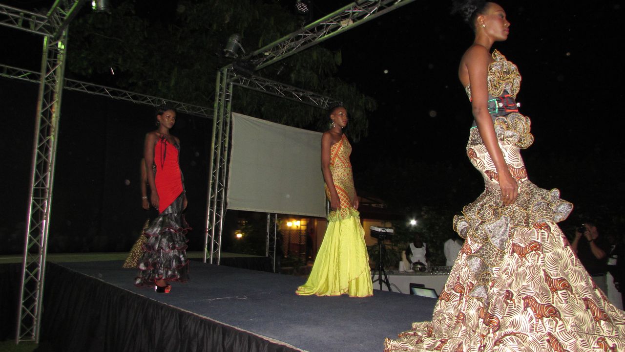 3 Modells in bunten Kleidern präsentieren sich auf dem Catwalk, sie sind von der Seite zu sehen.