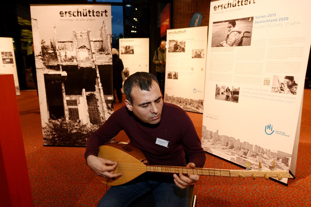 Mohamad Jolo, blinder Musiker aus Syrien, sitzt auf einem Stuhl in der Ausstellung und spielt das kurdische Instrument Saz.