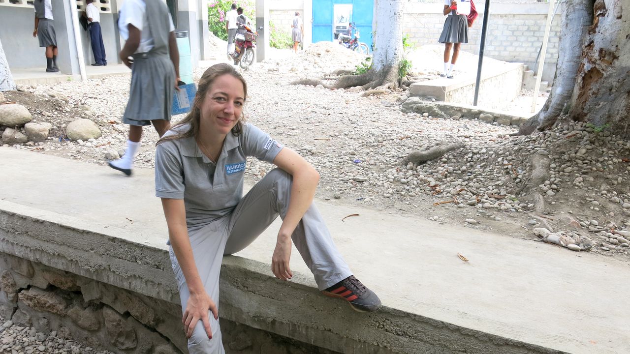 Aurelie sitzt auf einer Steinmauer im Schulhof, hinter ihr sieht man einige Schüler.