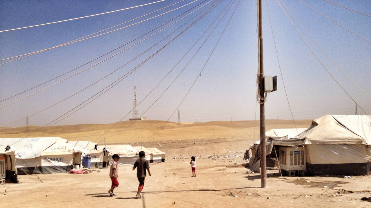 Einige Zelte stehen auf sandigem Boden. Einige Kinder rennen von der Kamera in Richtung Camp.