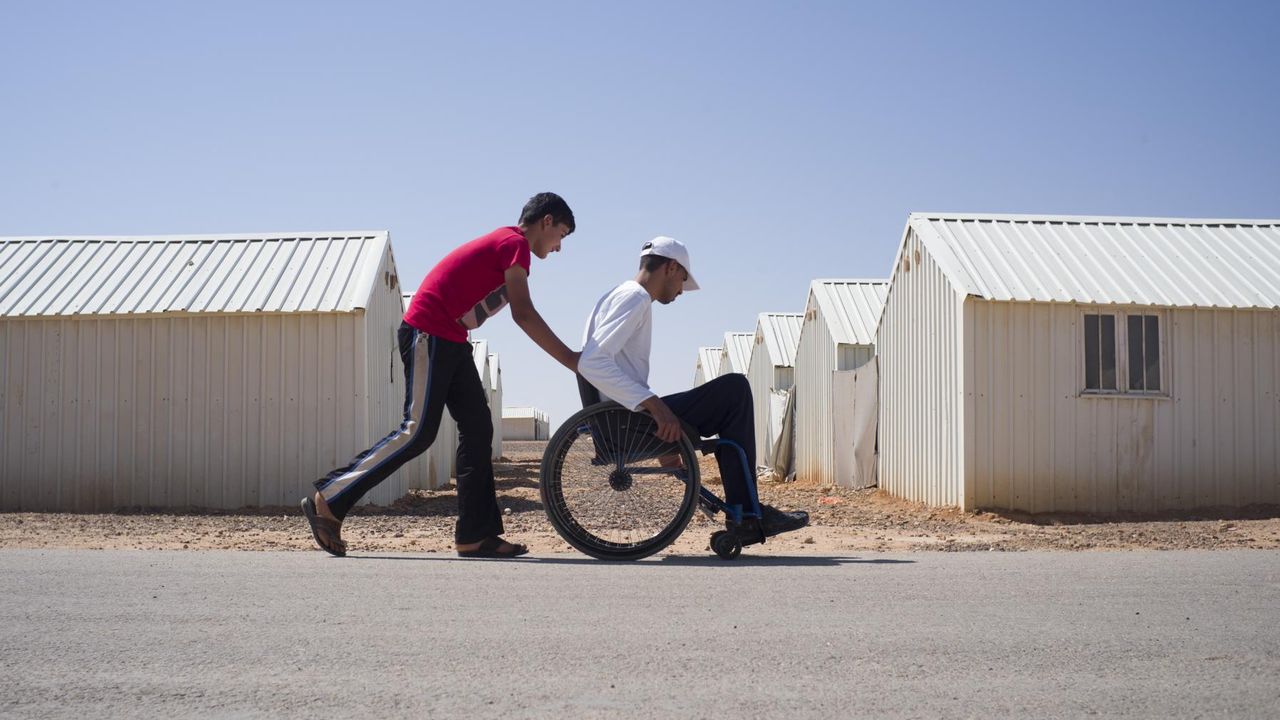Ein Mann schiebt seinen Nachbarn im Rollstuhl durch ein Flüchtlingscamp in Jordanien.