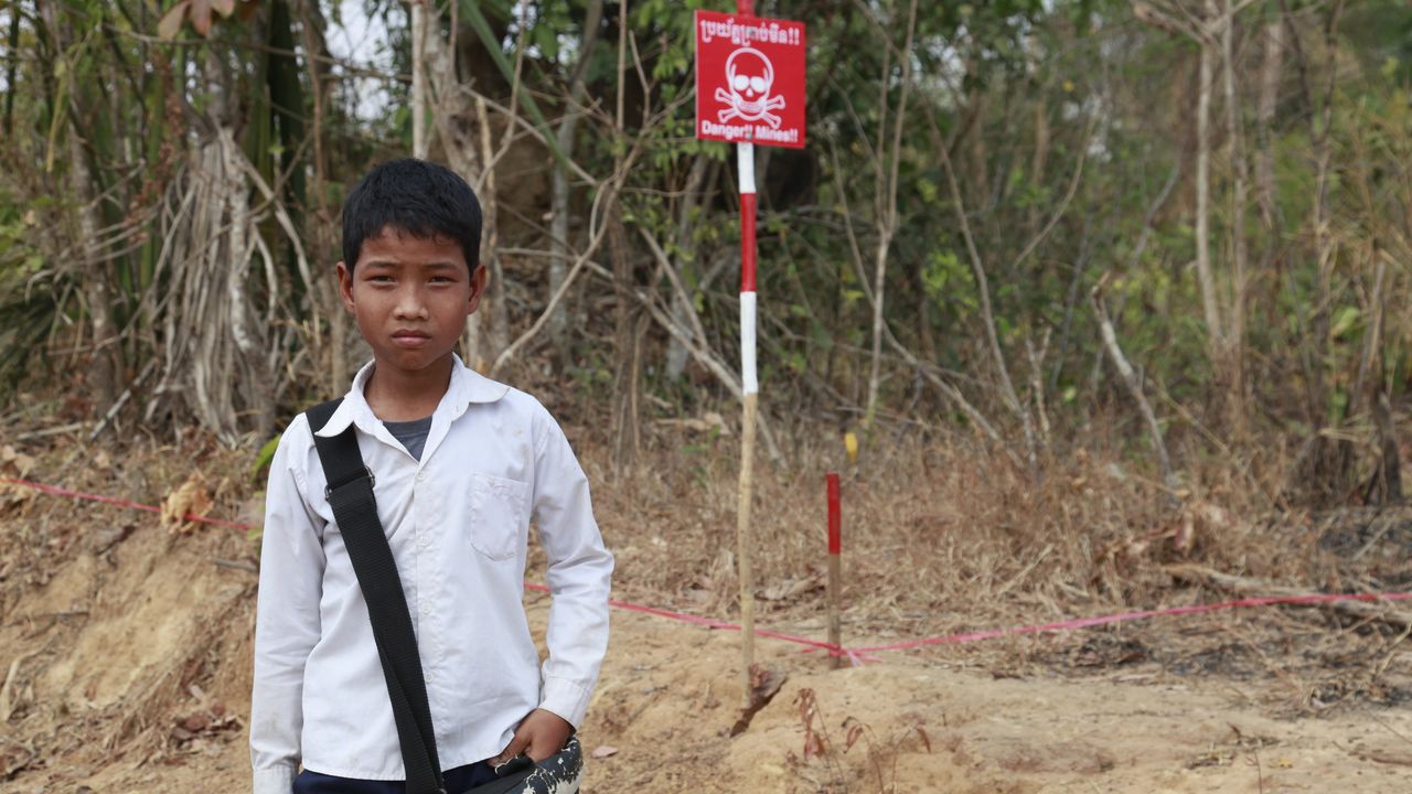 Ein Junge steht vor einem Danger Mines Schild auf einem Minenfeld in Kambodscha