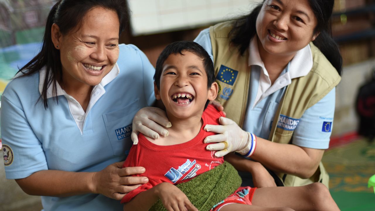 In einem Therapiezentrum in Myanmar lachen zwei Handicap International Mitarbeiter zusammen mit einem jungen Patienten.